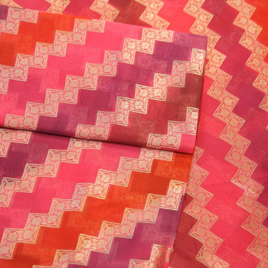 Luxurious pure organza fabric in gradient rangkaat tones with golden zigzag floral-bordered Zari weave.