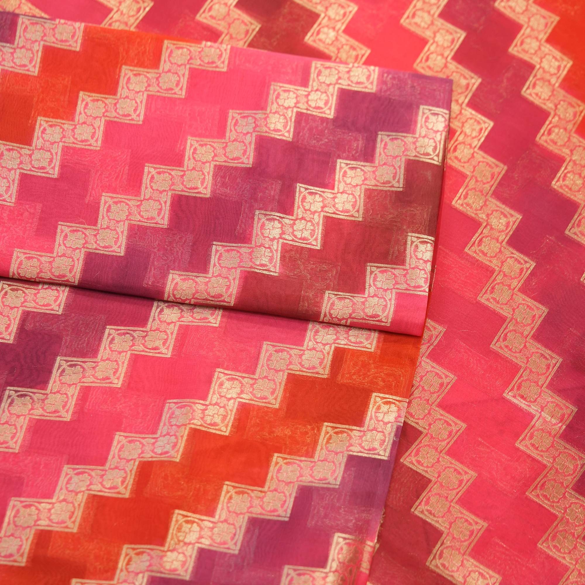 Luxurious pure organza fabric in gradient rangkaat tones with golden zigzag floral-bordered Zari weave.