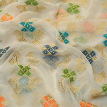 Sheer chiffon fabric with multicolored ikkat-style cotton floral motifs and shimmering golden zari weave on an off-white base.