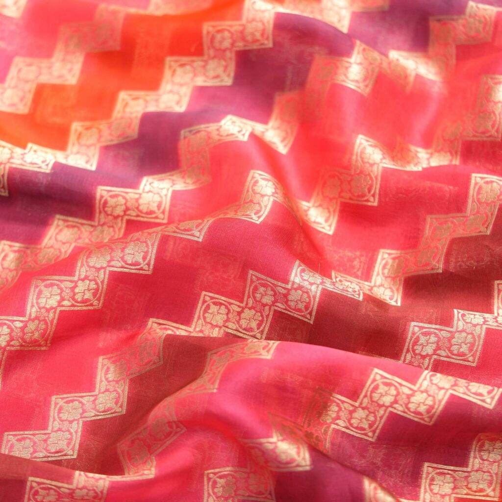 Luxurious pure organza fabric in gradient rangkaat tones with golden zigzag floral-bordered Zari weave.