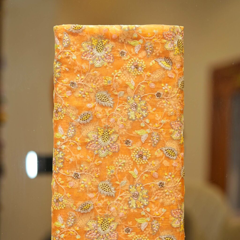 Golden orange pure organza fabric with intricate floral embroidery and shimmering crystal highlights – luxury festive material