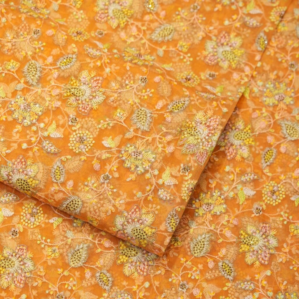 Golden orange pure organza fabric with intricate floral embroidery and shimmering crystal highlights – luxury festive material