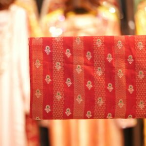 Rich red pure silk fabric with tissue jacquard stripes, golden zari weaving, and meenakari floral motifs